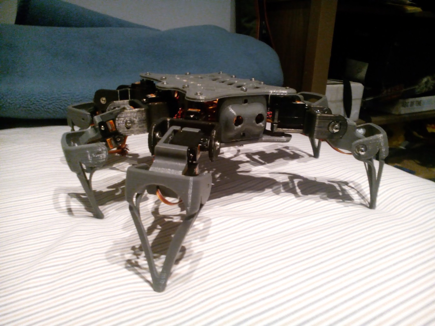 Robot hexápodo gris impreso en 3D, con patas de servos, sobre una cama