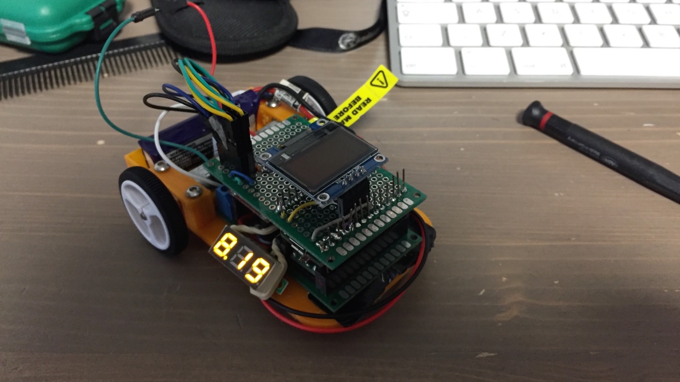Prototipo de SuperMaze: chasis naranja impreso en 3D con ruedas, una placa perforada con una pantalla OLED y un display de siete segmentos