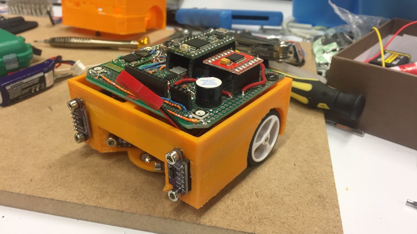 Prototipo de SuperMaze: caja naranja impresa en 3D con sensores de distancia en los laterales y una placa con el microcontrolador y un zumbador